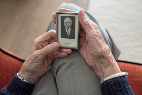 Picture of an older adult's hands holding an old photograph of their spouse